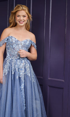 A young woman smiles at the camera in front of a dark purple paneled wall, wearing the Tiffany 16243 long prom dress—a light blue, off-the-shoulder gown with delicate floral embroidery.