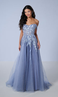 A woman wears the Tiffany 16243, a floor-length lavender prom dress with off-the-shoulder design, floral embroidery, and a sheer lace-detailed bodice, set against a plain background.