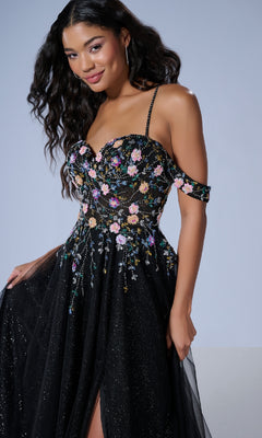A woman stands against a plain background wearing the Tiffany 16251 long prom dress, a black off-shoulder A-line gown with colorful floral embroidery, thin straps, and delicate floral beaded appliqué.