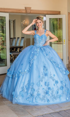 A woman stands outside double doors wearing the Quinceanera Dress 1627 By Dancing Queen, a light blue ball gown with floral details, a full tulle skirt, and a graceful sweetheart neckline.