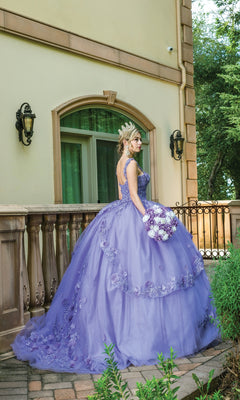 A woman in the Quinceanera Dress 1627 By Dancing Queen and a tiara stands on a stone patio, holding a bouquet of purple and white flowers, with floral details and greenery adding elegance to the scene.
