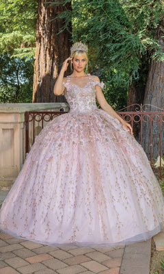 A person stands outdoors on a paved area, wearing the Quinceanera Dress 1640 By Dancing Queen—an off-the-shoulder pink a-line ball gown with floral details and a crown, with trees and a railing in the background.