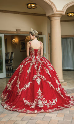 A person wearing the Quinceanera Dress 1651 by Dancing Queen, featuring red and gold lace with a sweetheart neckline and tiara, stands facing away in front of an arched entryway.