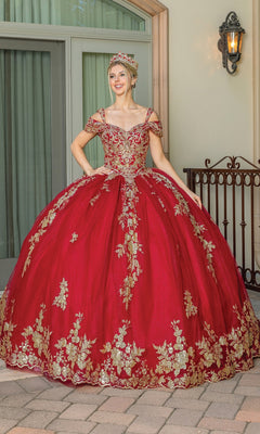 A woman poses outdoors in the Burgundy Red Quinceanera Dress 1657, featuring gold floral embroidery and a matching crown, smiling brightly at the camera.