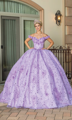 A person wearing the Quinceanera Dress 1660 By Dancing Queen, featuring off-the-shoulder floral details and a jeweled crown, stands outside on a brick patio in front of a building.