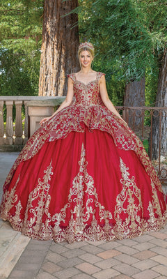 A person wearing the Quinceanera Dress 1670 By Dancing Queen—an ornate red and gold ball gown with gold lace embroidery and a matching crown—stands outdoors by trees and stone railings.