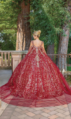 A woman in the Quinceanera Dress 1670 by Dancing Queen stands on a stone terrace, facing away, surrounded by lush greenery.