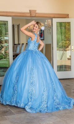 A woman in the Quinceanera Dress 1678 by Dancing Queen, featuring blue floral details and removable draped sleeves, stands before open glass doors, smiling over her shoulder.