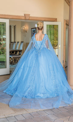 A woman in the Quinceanera Dress 1678 by Dancing Queen, a light blue floor-length A-line gown with lace details and removable draped sleeves, stands with her back to the camera facing a dining room doorway.
