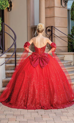 A woman stands on a brick path facing a staircase, her back to the camera, showcasing the elegant Quinceanera Dress 1683 By Dancing Queen—a sparkling red bow-back strapless ball gown.
