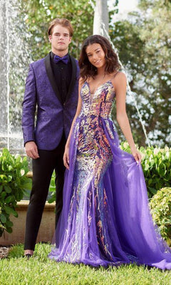 A young man in a purple tuxedo and a young woman wearing the Long Sequin Prom Dress: Tiffany 16944 with a tulle overlay pose outdoors by a fountain.
