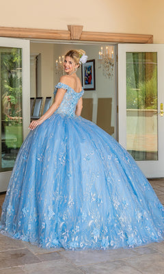 A woman wearing the Quinceanera Dress 1694 By Dancing Queen—a light blue, off-the-shoulder ball gown with floral accents and a sweetheart neckline—stands before glass doors, smiling over her shoulder.