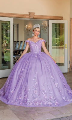 A person wearing the Quinceanera Dress 1698 By Dancing Queen, a detailed floral ball gown with a sweetheart neckline, and a tiara stands in front of open glass doors.