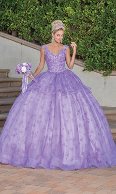 A woman wearing the Quinceanera Dress 1702 By Dancing Queen—a lavender ball gown with a full skirt and lace embellished cape—stands outdoors holding a matching bouquet, with greenery and steps in the background.
