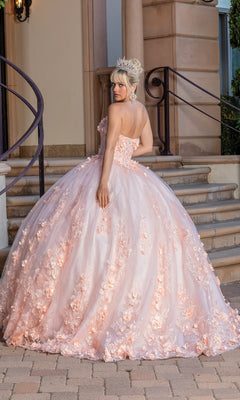 A woman wears the Pastel Peach Quinceanera Dress 1705 with a sweetheart strapless neckline and floral embroidery, standing on steps outside, silver tiara on her head as she looks over her shoulder.