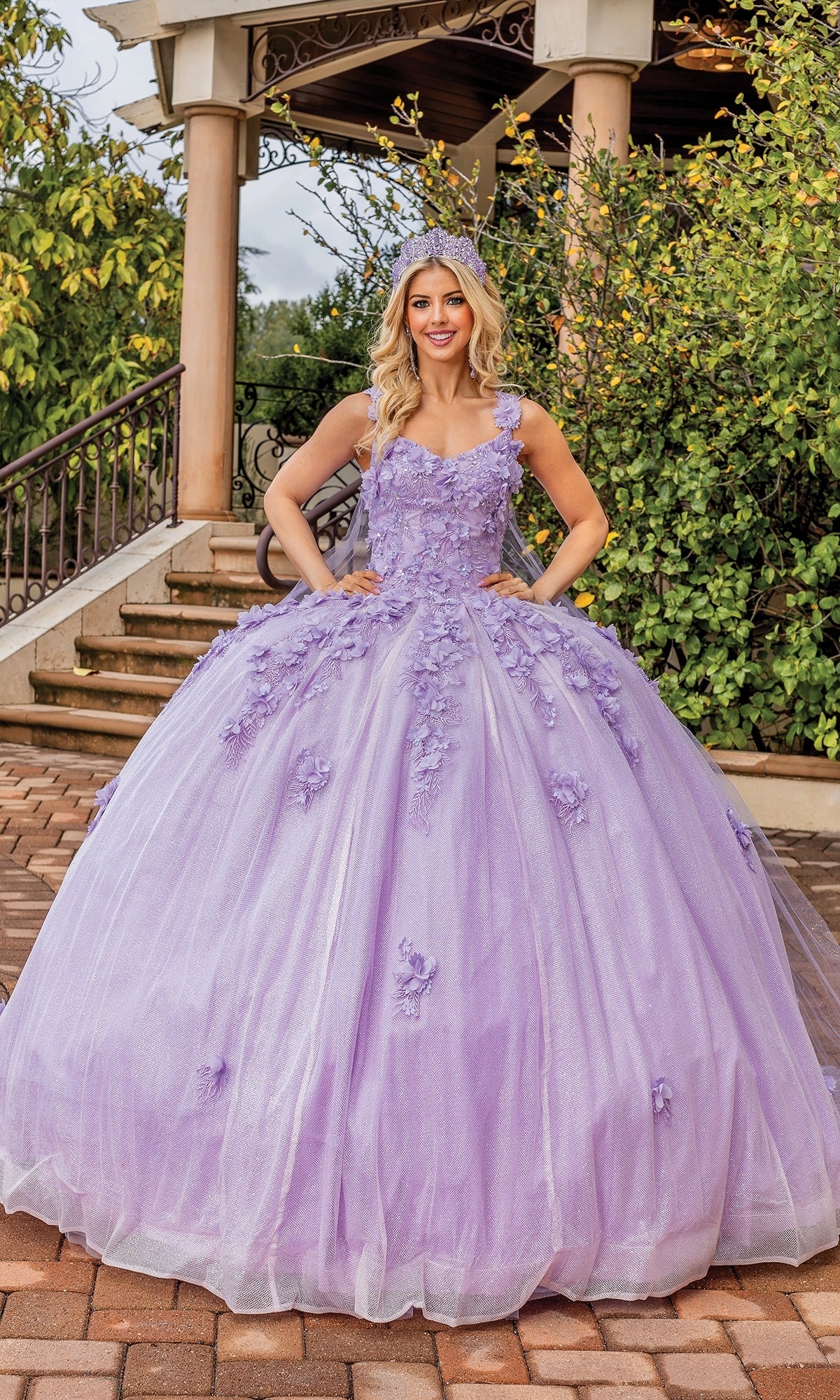A woman wearing the Quinceanera Dress 1707 By Dancing Queen with a tiara stands outdoors in front of a staircase and gazebo.