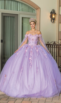 A woman in the Quinceanera Dress 1714 By Dancing Queen, a pastel purple ball gown with floral details and a tiara, stands before a building with large windows and a wrought iron fence.