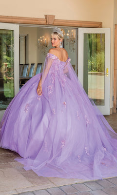 A woman in the Quinceanera Dress 1714 By Dancing Queen and a tiara stands outdoors, facing away, with glass doors and chandeliers visible in the background.