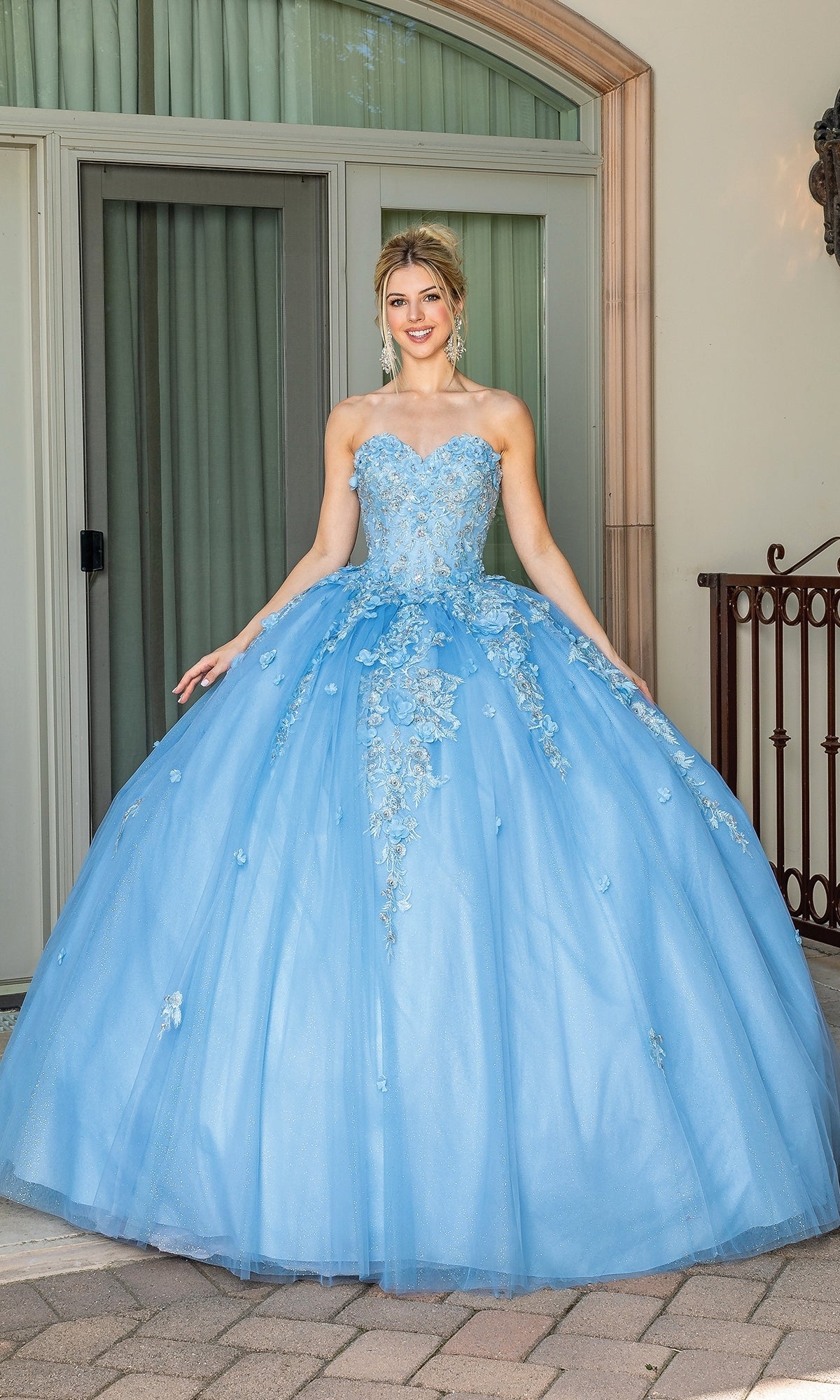 A woman stands outside in the Strapless Blue Quinceanera Dress 1717, featuring a pastel blue hue, strapless sweetheart neckline, floral embroidery, and a full tulle skirt.