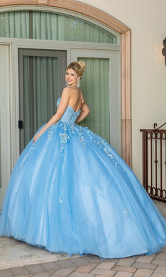 A woman wearing the Strapless Blue Quinceanera Dress 1717 with a sweetheart neckline stands outdoors in front of large glass doors, looking over her shoulder and smiling.