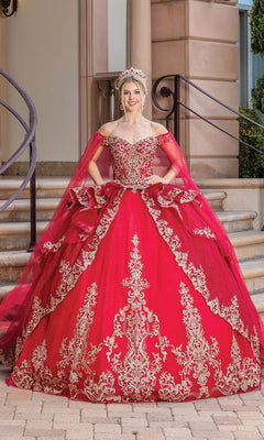 A woman stands on steps wearing the Quinceanera Dress 1720 By Dancing Queen, an off-the-shoulder bright red ball gown with gold embroidery, a matching cape, and a jeweled crown.