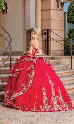 A young woman in the Quinceanera Dress 1720 by Dancing Queen, a bright red off-the-shoulder gown with gold embroidery, stands on a stone patio, glancing over her shoulder at the camera.