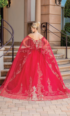 Wearing the Quinceanera Dress 1720 By Dancing Queen, a person in an off-the-shoulder red ball gown with gold embroidery and a long sheer cape stands on stone steps, facing away from the camera.