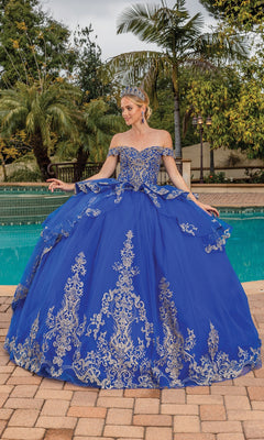 A woman in the Quinceanera Dress 1720 By Dancing Queen, featuring off-the-shoulder gold fabric with blue and gold embroidery and a tiara, stands by a pool outdoors, surrounded by lush greenery and trees.