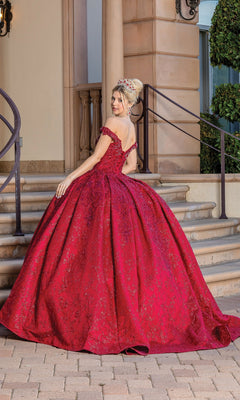 Wearing the Burgundy Red Quinceanera Dress 1722 with a full skirt and off-the-shoulder sleeves, a woman stands on stone steps, facing away. Her hair is styled up and topped with a crown.