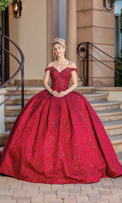 A woman stands on steps wearing the Burgundy Red Quinceanera Dress 1722, an ornate off-the-shoulder ball gown with a full skirt and jeweled tiara.