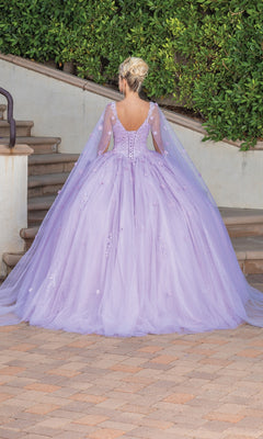 A person with blonde hair in an updo wears the Quinceanera Dress 1731 By Dancing Queen—a lilac ball gown with a full skirt, sheer cape, and sweetheart neckline—while standing on a brick path near stairs and greenery.