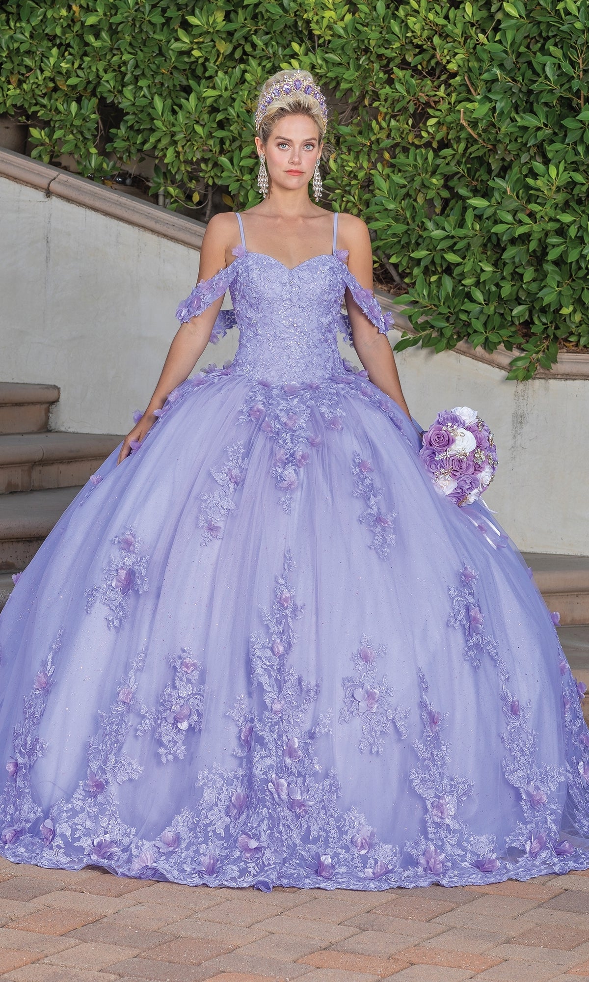 A young woman stands outdoors in the Quinceanera Dress 1747 By Dancing Queen, featuring lilac floral details and a matching tiara, holding a round bouquet with green bushes and steps in the background.