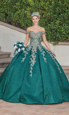 A woman wearing the Quinceanera Dress 1753 By Dancing Queen—an emerald green, off-the-shoulder gown with silver embellishments and lace embroidery—stands outdoors with a matching tiara and bouquet in front of lush greenery and steps.