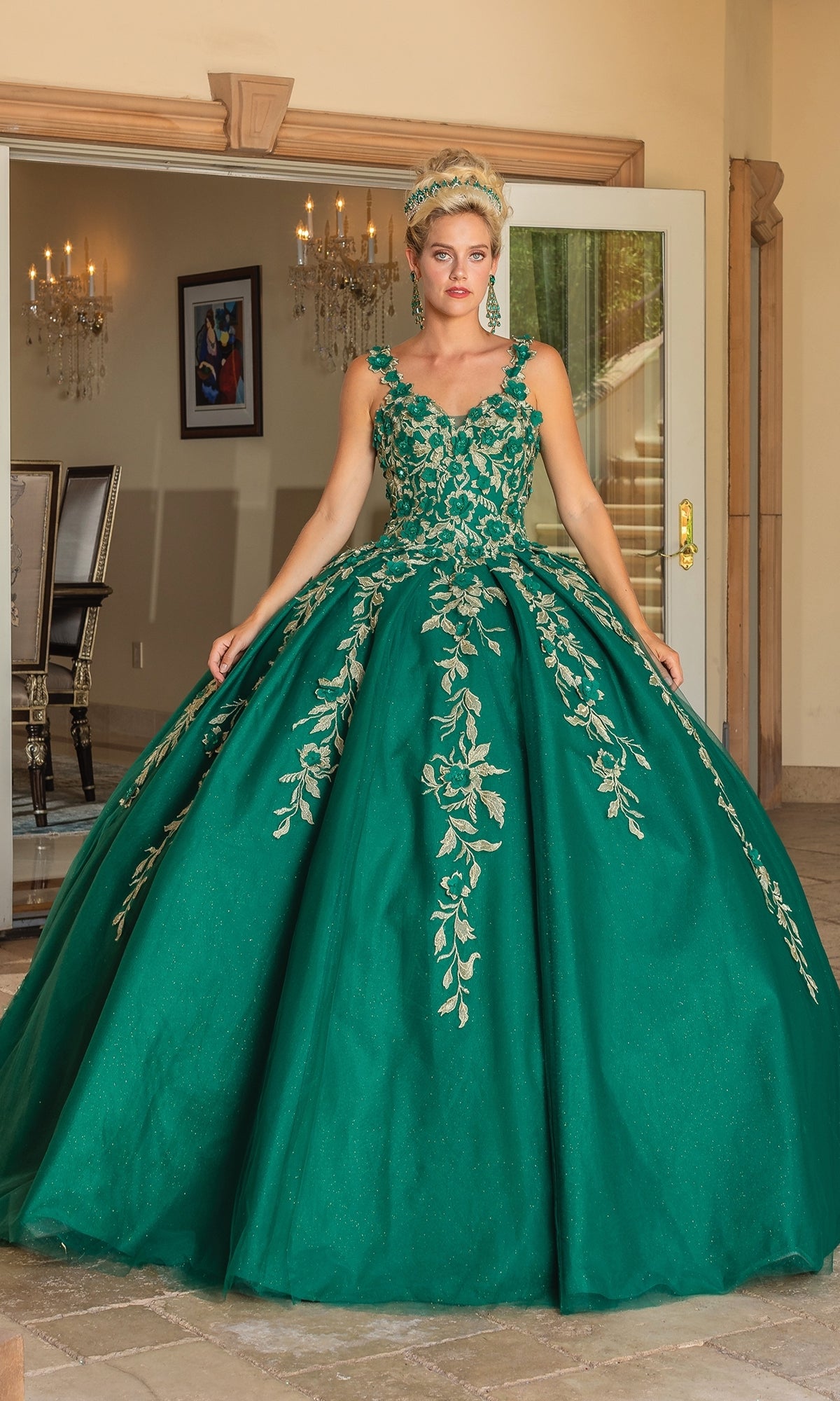 A woman indoors wears the Quinceanera Dress 1755 by Dancing Queen, a floor-length hunter green gown with gold floral embroidery, a full skirt, and an elegant a-line ball gown silhouette.