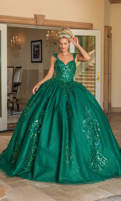 A woman poses by open glass doors, wearing the Quinceanera Dress 1758 By Dancing Queen—an emerald green A-line ball gown with sparkling glitter lace embroidery and one hand elegantly raised near her head.