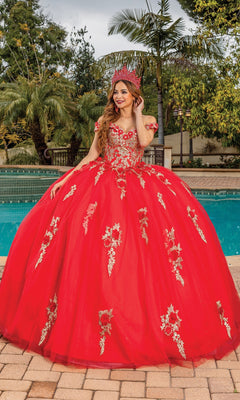 A young woman wears the Quinceanera Dress 1760 By Dancing Queen—a bright red a-line ball gown with gold floral embroidery and a matching crown—while standing by a pool amid lush greenery.