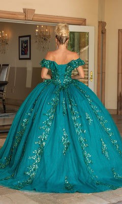 A woman stands indoors facing away, wearing the Quinceanera Dress 1766 By Dancing Queen—an a-line teal ball gown with off-the-shoulder sleeves, floral embellishments, and a full skirt.