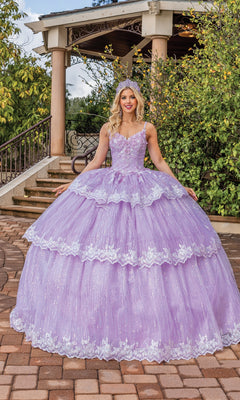 A woman stands outdoors in front of a gazebo and greenery, wearing the Quinceanera Dress 1770 By Dancing Queen—a lavender a-line ball gown with off-the-shoulder straps, lace details, voluminous skirt, and tiara.