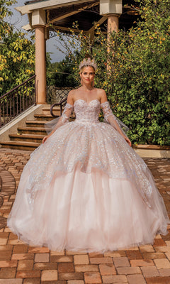 A woman in the Quinceanera Dress 1773 By Dancing Queen—sparkling, light pink, strapless with removable sheer sleeves and a tiara—stands outdoors on a paved walkway before steps and greenery.
