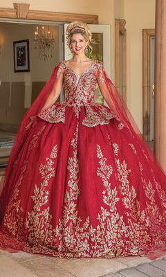 A woman smiles at the camera indoors wearing Dancing Queen's Quinceanera Dress 1781, a burgundy gown with gold embroidery, sheer cape sleeves, and a gold tiara.