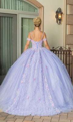 A person stands outdoors facing away, wearing the Quinceanera Dress 1785 By Dancing Queen—a lilac ball gown with floral details and off-the-shoulder straps—hair elegantly styled in an updo.