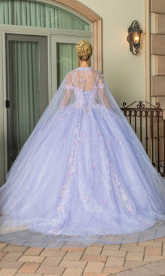 A woman stands outside facing away, wearing the Quinceanera Dress 1785 By Dancing Queen—a lilac ball gown with floral details, a sheer cape, and a sweetheart neckline—by a glass door.
