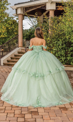 A person wears the Quinceanera Dress 1788 by Dancing Queen—a light green, off-the-shoulder sweetheart ball gown—on a brick pathway with a gazebo and greenery behind them.