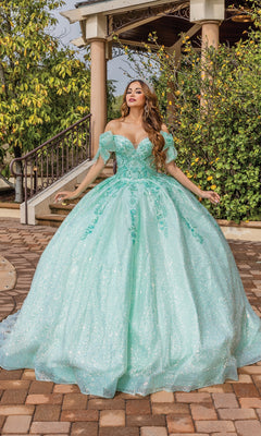A woman poses gracefully outdoors in front of a garden gazebo wearing Quinceanera Dress 1804 By Dancing Queen, a sparkling mint green off-the-shoulder gown with a full skirt and sweetheart neckline.