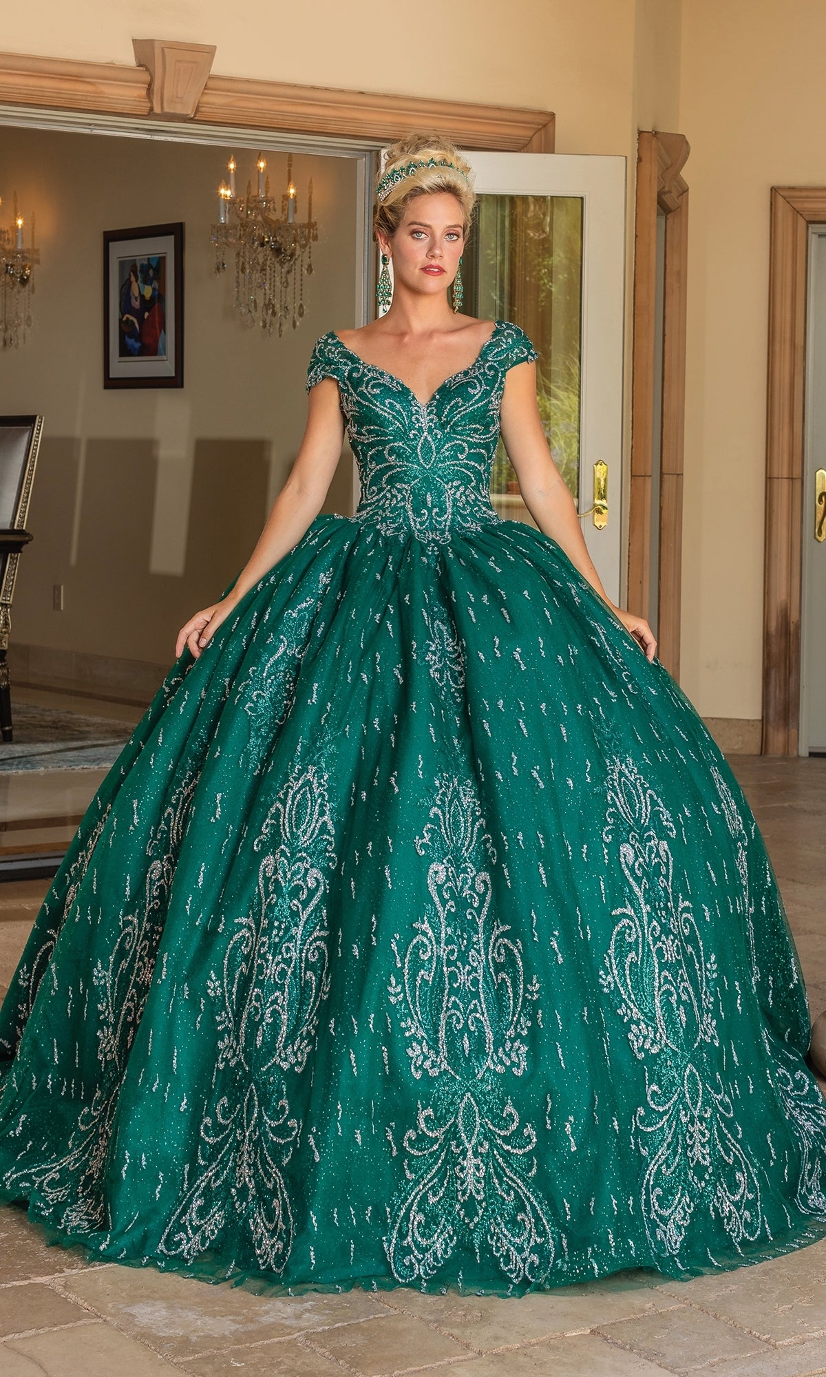 A woman stands indoors wearing the Quinceanera Dress 1805 By Dancing Queen, featuring hunter green fabric, intricate silver embroidery, a sweetheart neckline, and a full, voluminous skirt.