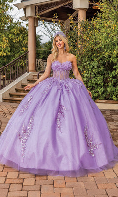 A woman poses outdoors near lush greenery and a pavilion, wearing the Quinceanera Dress 1813 By Dancing Queen— a pastel ball gown with floral embellishments, sweetheart neckline, and tiara.