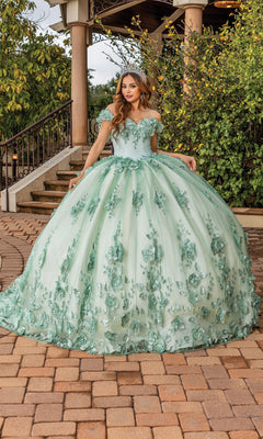A woman stands outdoors on a stone path near greenery and a gazebo, wearing the Quinceanera Dress 1818 by Dancing Queen—a light green ball gown with floral appliqué, sweetheart neckline, and tiara.