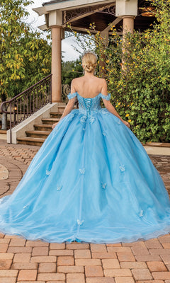A woman wearing the Quinceanera Dress 1826 by Dancing Queen, an a-line ball gown with butterfly details, stands outdoors near a staircase and greenery, facing away from the camera.