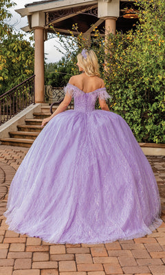 A woman wearing the Quinceanera Dress 1829 By Dancing Queen, an off-the-shoulder lavender ball gown with a sweetheart neckline, stands outdoors with her back to the camera near stone steps and lush greenery.