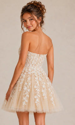 A woman is standing and looking over her shoulder against a plain background, wearing the Jovani 1830 short homecoming dress—a strapless fit-and-flare beige style adorned with white floral lace appliques.
